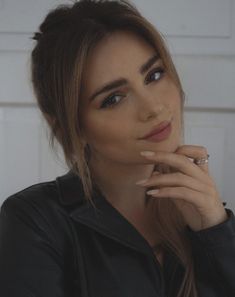 a close up of a person wearing a black shirt and holding her hand near her face