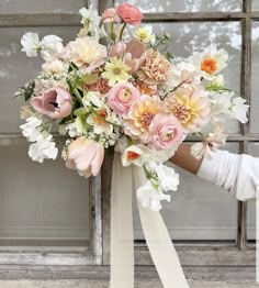 a bridal bouquet in front of a window with white ribbon and flowers on it