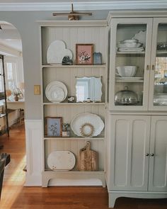 a white china cabinet filled with plates and other items on top of wooden flooring