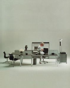 a person sitting at a desk in front of a computer monitor and keyboard with chairs around it