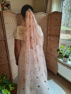 a woman in a white dress is wearing a pink veil and looking out the window