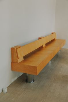 a wooden bench sitting on top of a hard wood floor next to a white wall