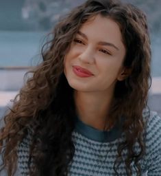 a woman with long curly hair wearing a blue and white striped sweater looking at the camera