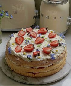 a cake with strawberries on it sitting on a table next to two toasters