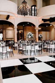 a banquet hall with black and white checkered flooring, chandeliers and tables