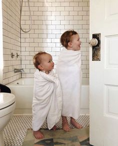 two young children wrapped in white towels standing next to each other on the bathroom floor