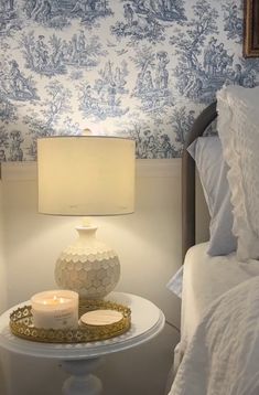 a white table with a lit candle on it in front of a blue and white wallpaper