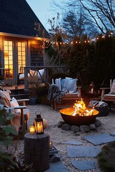 a fire pit surrounded by chairs and lights in a backyard with gravel path leading up to the house