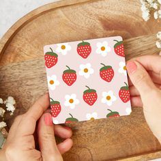 two hands holding a card with strawberries and daisies on it next to flowers