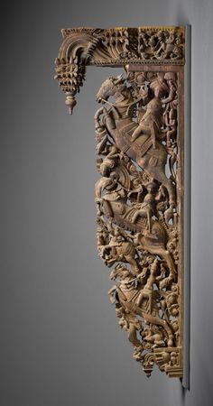 an intricately carved wooden wall hanging on the side of a gray wall with grey walls