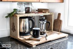 a coffee maker and two mugs on a wooden tray