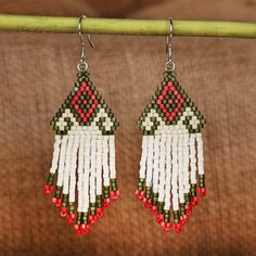 the beaded earrings are hanging from a wooden hook on a green stick with a brown background