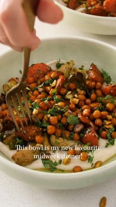 a person is holding a fork over a bowl of food with chickpeas and carrots