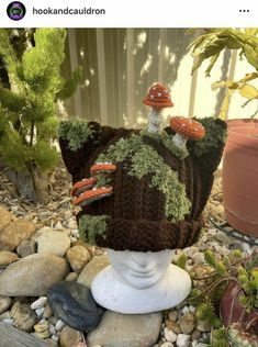 a knitted mushroom hat sitting on top of a white vase filled with rocks and plants