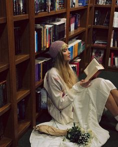 a woman sitting on the floor in front of a book shelf with books and flowers