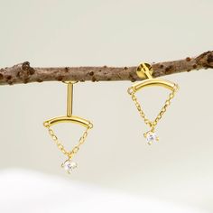 two pairs of gold earrings hanging from a tree branch with white stones in the middle