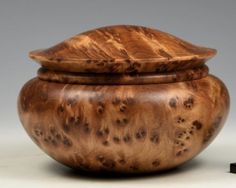 a wooden bowl with lid sitting on top of a white table next to a black object