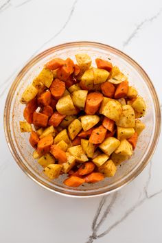 a glass bowl filled with cooked carrots on top of a white countertop next to a marble table