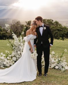 a bride and groom standing in front of white flowers at their wedding ceremony with the sun shining down on them