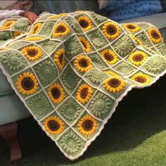 a crocheted blanket with sunflowers on it is sitting on the grass