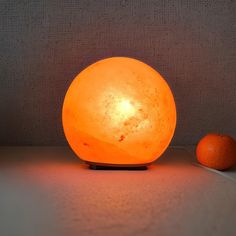 an orange sitting on the floor next to a light that looks like it has been turned on