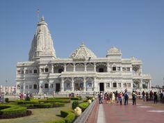 people are walking around in front of a white building that is surrounded by greenery