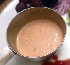 a bowl of soup sitting on top of a white plate next to grapes and lettuce