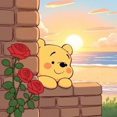 a teddy bear sitting on top of a brick wall next to a red rose with the ocean in the background