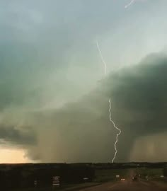 a lightning bolt is seen in the sky above a road with cars driving on it