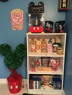 a book shelf filled with lots of movies and snacks next to a potted plant