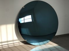 a large round mirror sitting on top of a white wall next to a window in a room