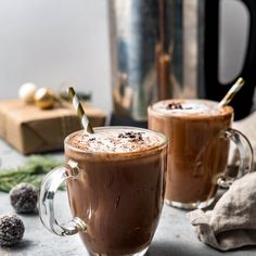 two mugs filled with hot chocolate on top of a counter next to a blender