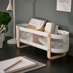 a desk with a pen, notebook and paper holder on it next to a lamp