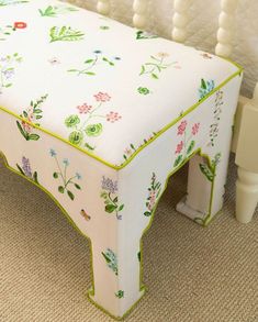 a white bench with green trim and flowers on it's sides, in front of a beige carpet