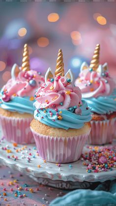 three cupcakes with pink, blue and gold frosting on a white plate