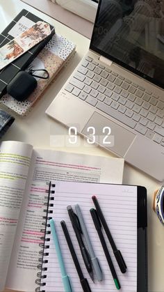 an open laptop computer sitting on top of a desk next to notebooks and pens