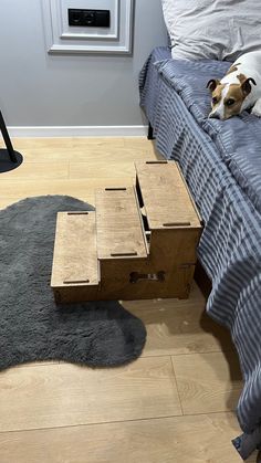 a dog laying on top of a bed next to a night stand with drawers under it