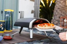 a pizza is being cooked in an outdoor oven on a wooden table next to other food items