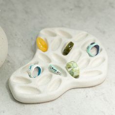 a white vase sitting on top of a table next to a ceramic object with different colored stones