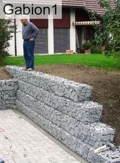 a man standing on top of a stone wall in front of a house next to a garden