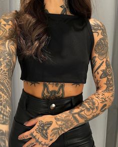 a woman with tattoos on her arms and chest is wearing black leather pants, a crop top