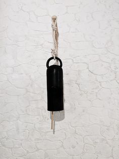 a black object hanging from a rope on a white brick wall with knots attached to it