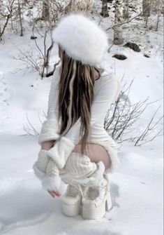 a woman with long hair wearing white boots and a fur hat sitting in the snow