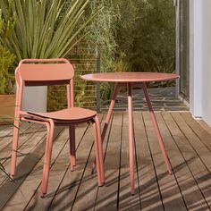 two pink chairs and a table on a wooden deck with plants in the back ground