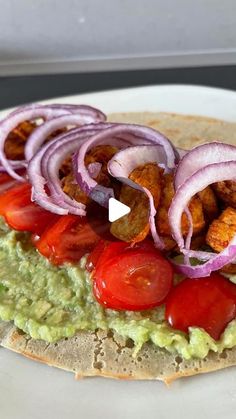 a tortilla with guacamole, tomatoes and onion on it sitting on a white plate