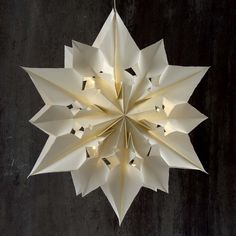 an origami style light fixture hanging from a black wall with white paper on it