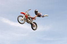 a man flying through the air on top of a dirt bike in front of a blue sky