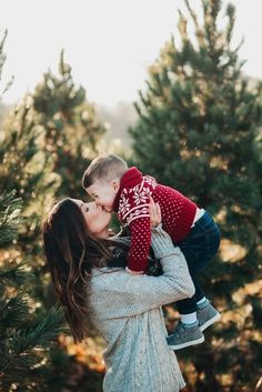 a mother kissing her son in front of christmas trees