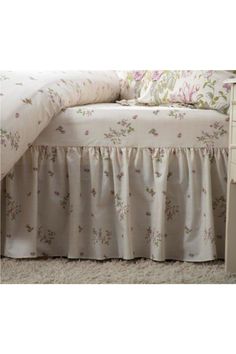 the bed is made up with white sheets and pink flowers on it's ruffled bedskirt