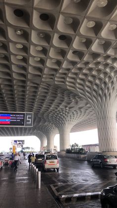 cars parked in front of an airport terminal with multiple columns on the ceiling and people walking by